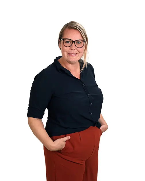 Lachende blonde vrouw met een rode broek en zwarte top, met haar handen in de zakken.