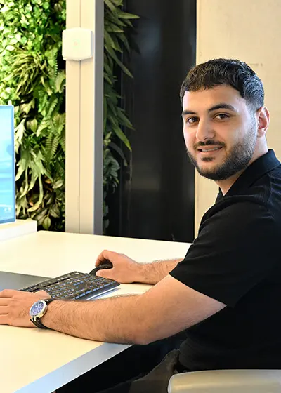 Man met zwarte polo en baard aan een bureau.