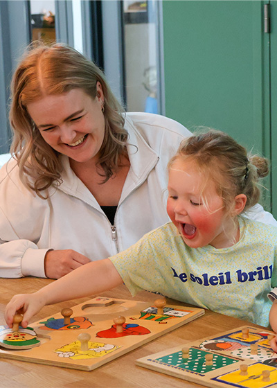 Vrouw in wit vest en jong meisje spelen met puzzel.