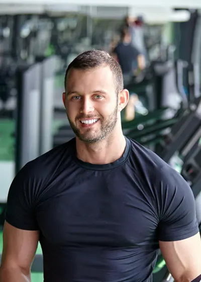 Lachende gespierde man, met sportschool als achtergrond.