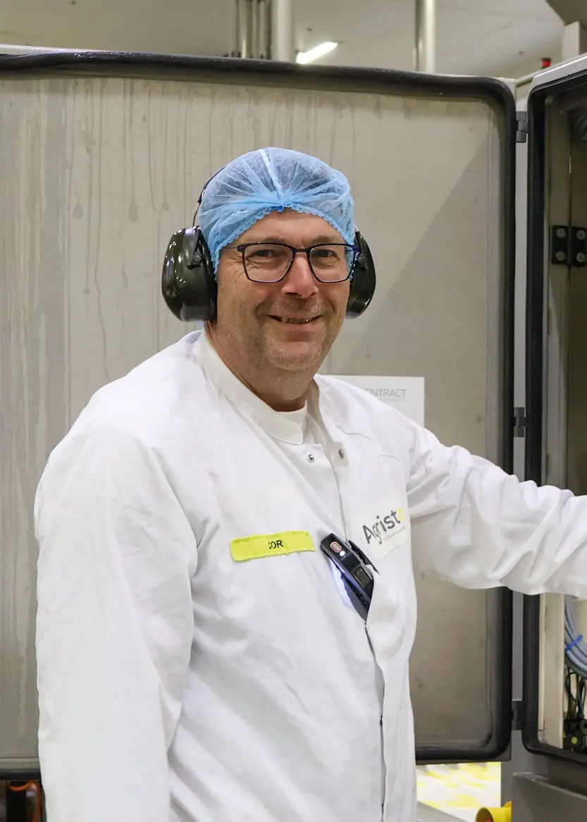 Man in witte laboratoriumjas en blauw hoofdnetje in een fabriek.