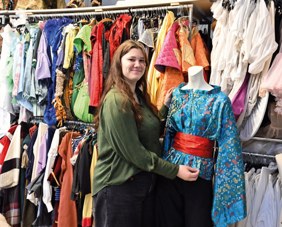 Vrouw in groene blouse in ruimte met kleding en staat voor een paspop met blauwe blouse.
