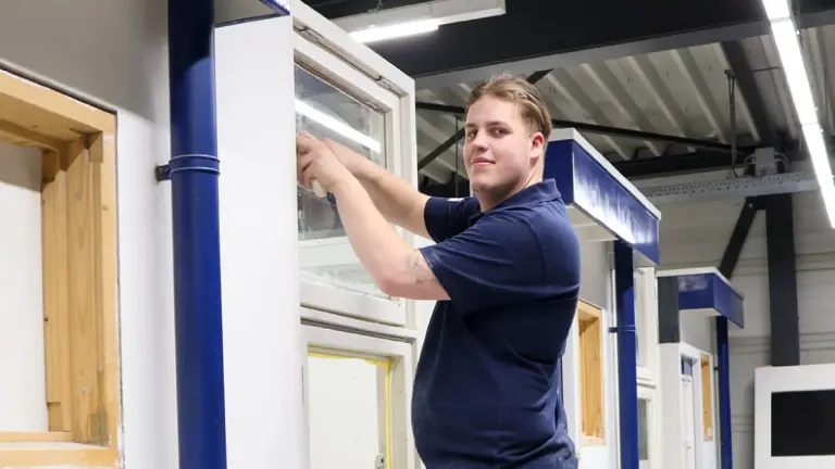 Man in donkerblauwe polo aan het werk in werkruimte.