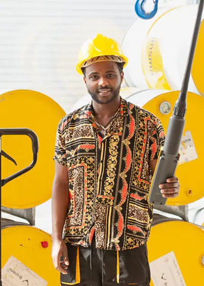 Man in werkkleding en veiligheidshelm, met gele tonnen in de achtergrond.