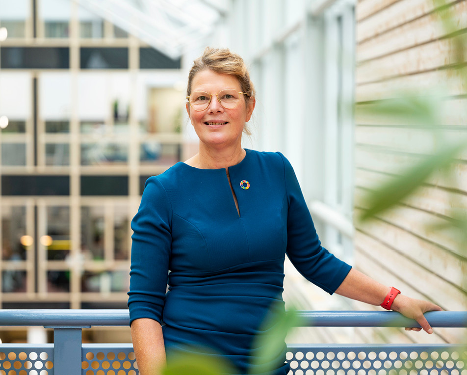 Vrouw in blauwe jurk staat in een lichte ruimte.