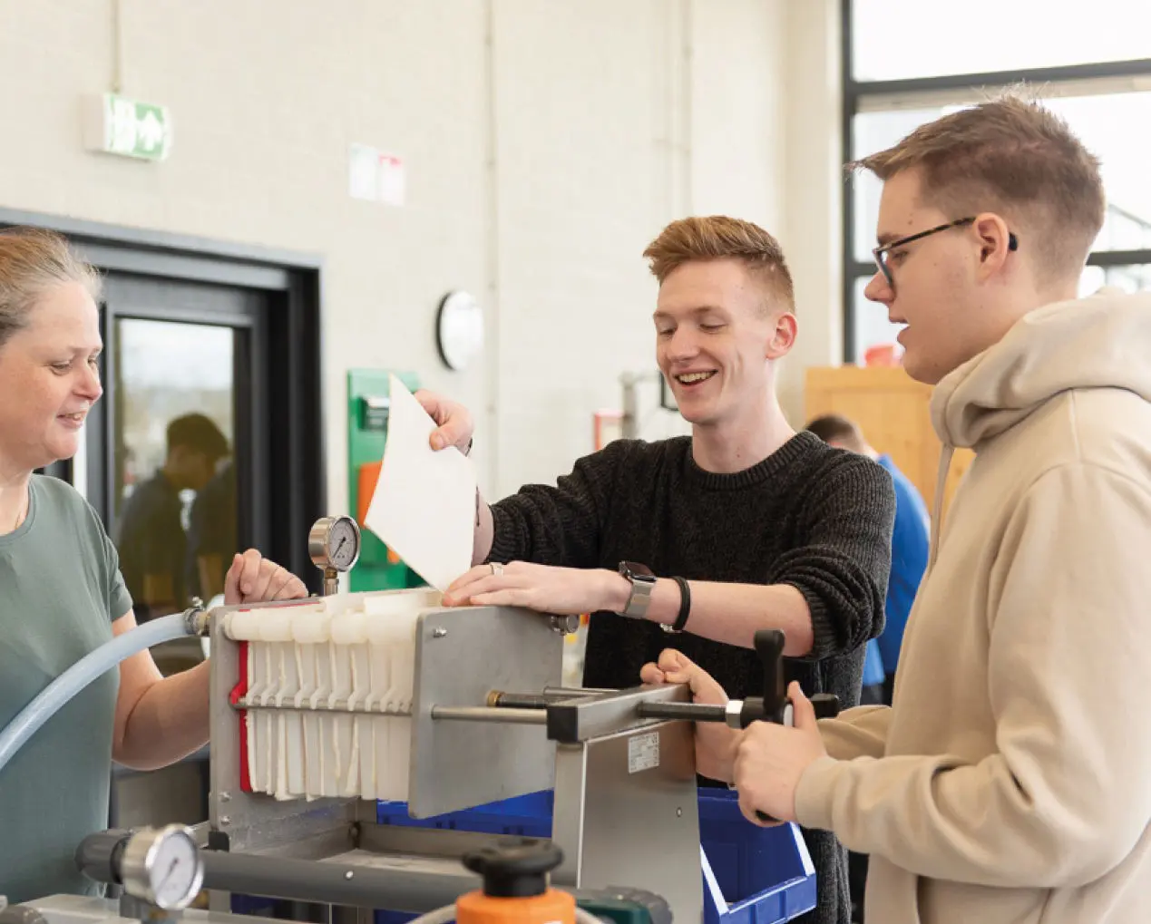 Drie mensen werken in een werkplaats, waarbij één persoon een vel papier vasthoudt.