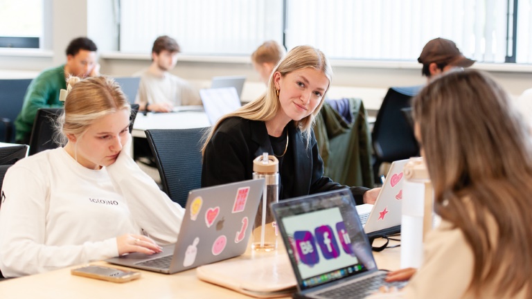 Klaslokaal met studenten die aan hun laptop werken.