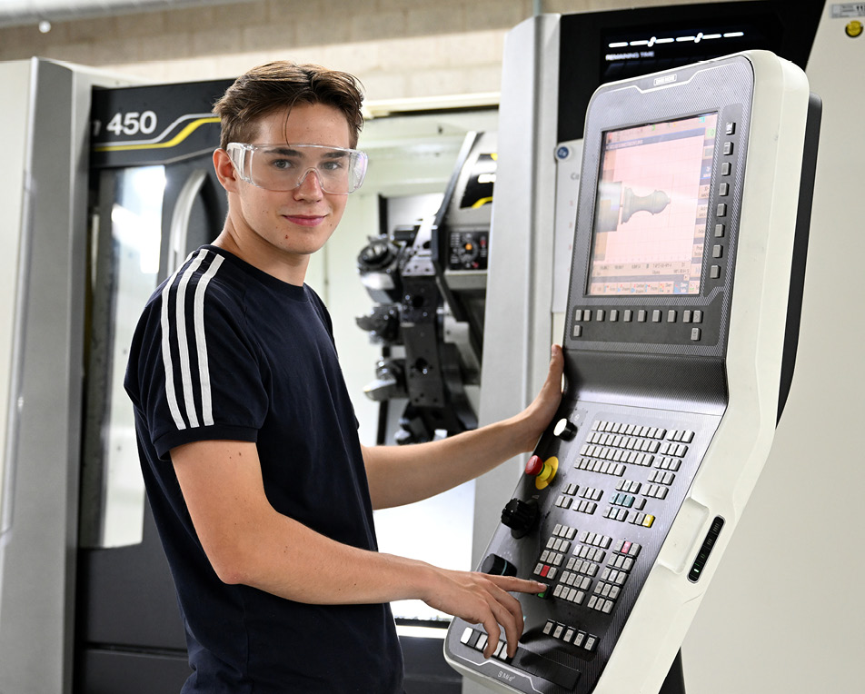 Persoon bedient een CNC-machine via een bedieningspaneel met scherm en knoppen.