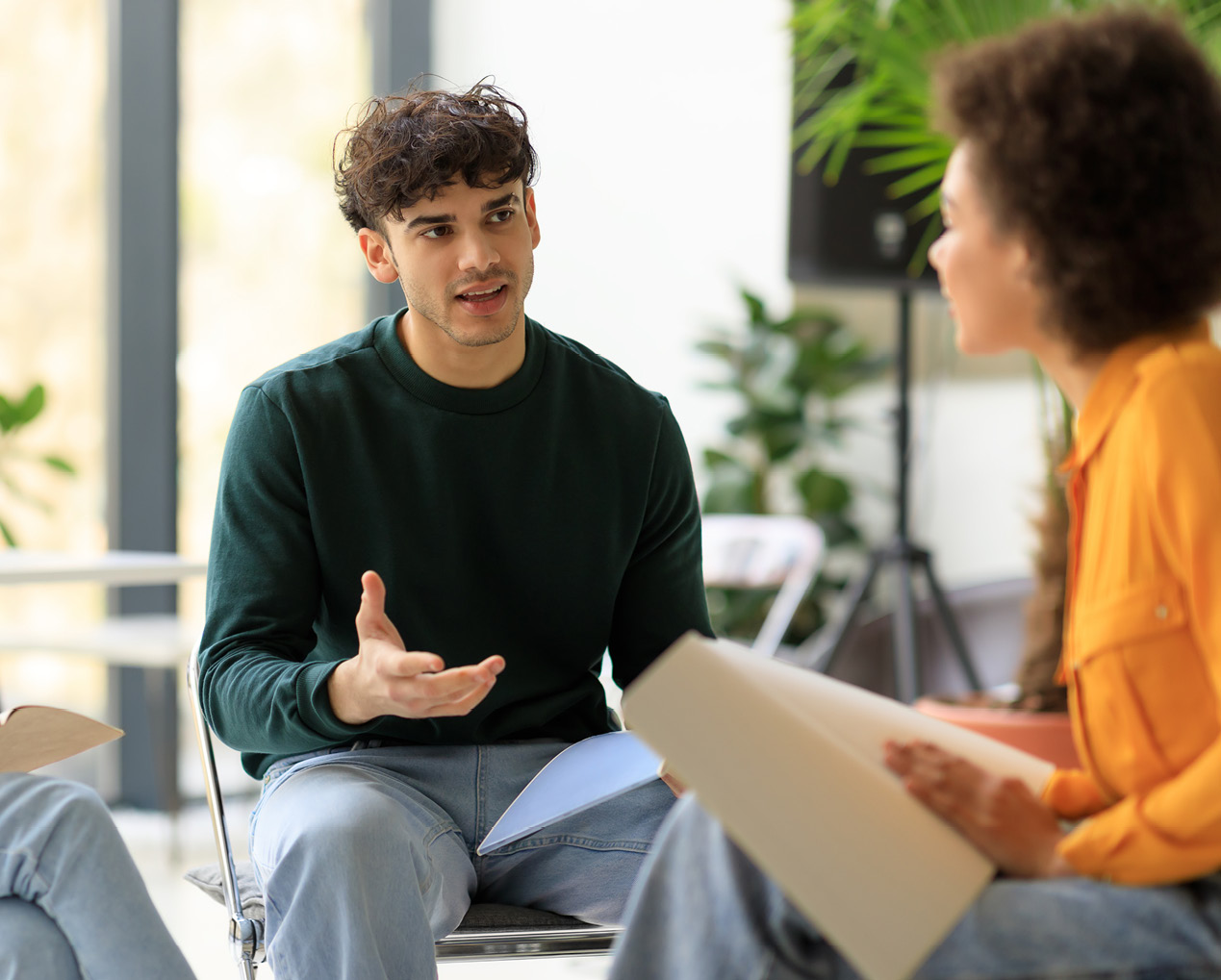 Man in een groene trui praat zittend met twee andere personen
