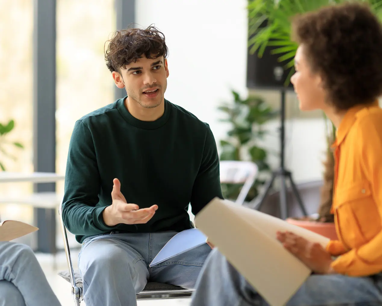 Man in een groene trui praat zittend met twee andere personen