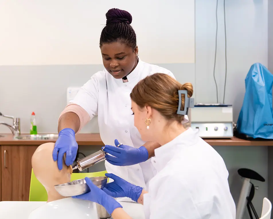Twee personen in witte jassen werken met een medisch oefenpop in een klinische opleidingsruimte.