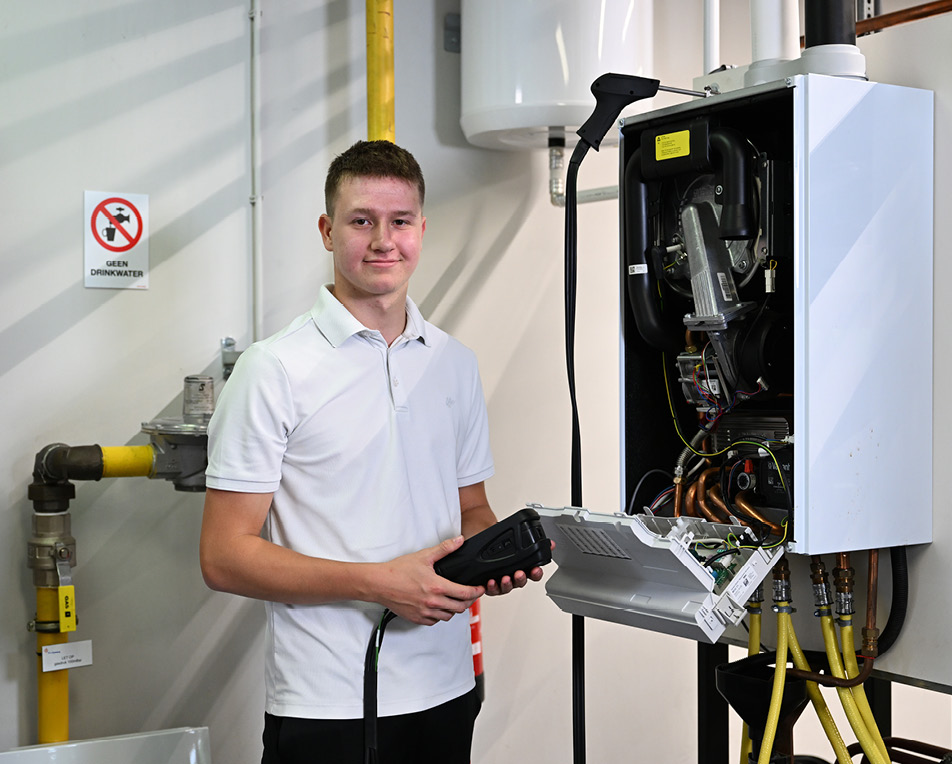 Persoon in witte polo inspecteert een open boiler met een diagnosetool