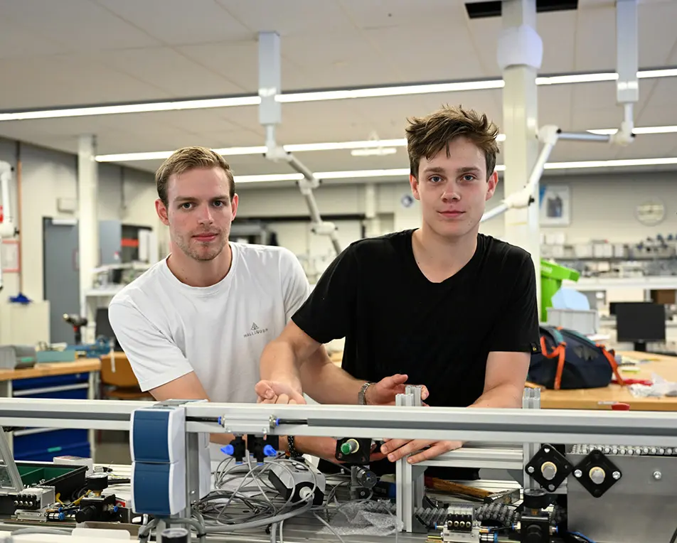 Man in donkere outfit staat in een werkplaats en is bezig met buizen