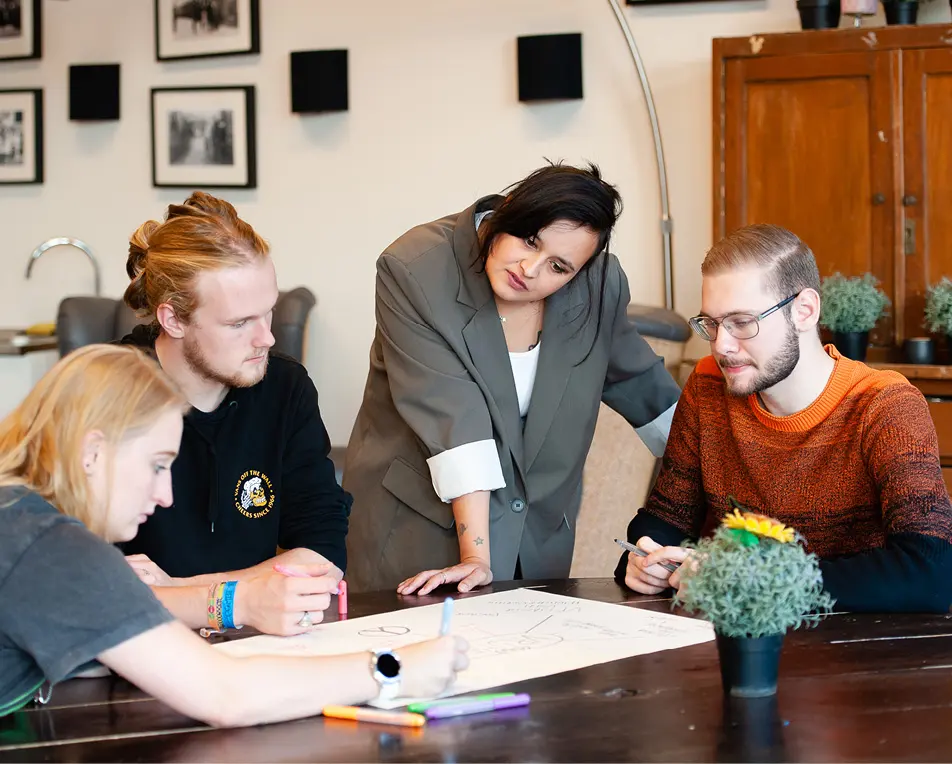 Vier personen werken samen aan een project rond een tafel met een groot vel papier en tekenmateriaal.