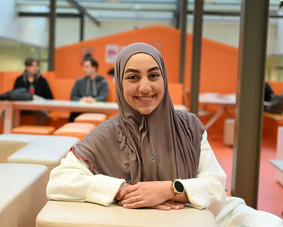 Persoon met hoofddoek zit in een binnenruimte met oranje meubilair