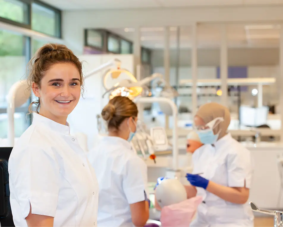 Personen in witte jassen werken met tandheelkundige oefenpoppen in een trainingsruimte.