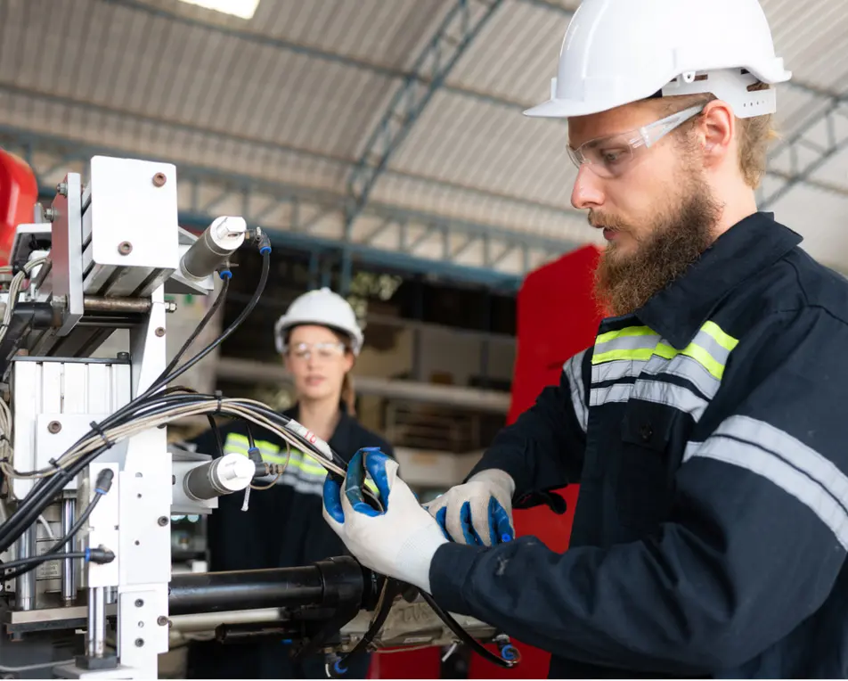 Twee personen staat met veiligheidshesje en veiligheidshelmen in een lichte gang met draden