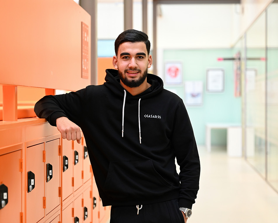 Persoon met zwarte hoodie leunt tegen een rij oranje lockers