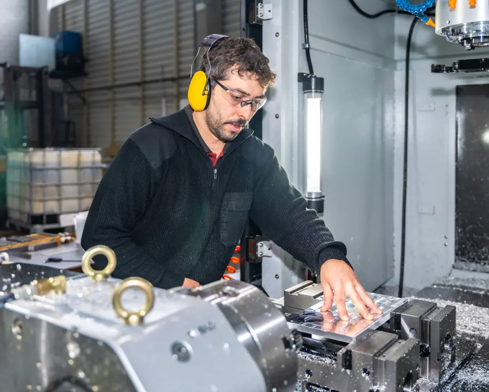Man met gele koptelefoon in werkruimte bezig met metaal.
