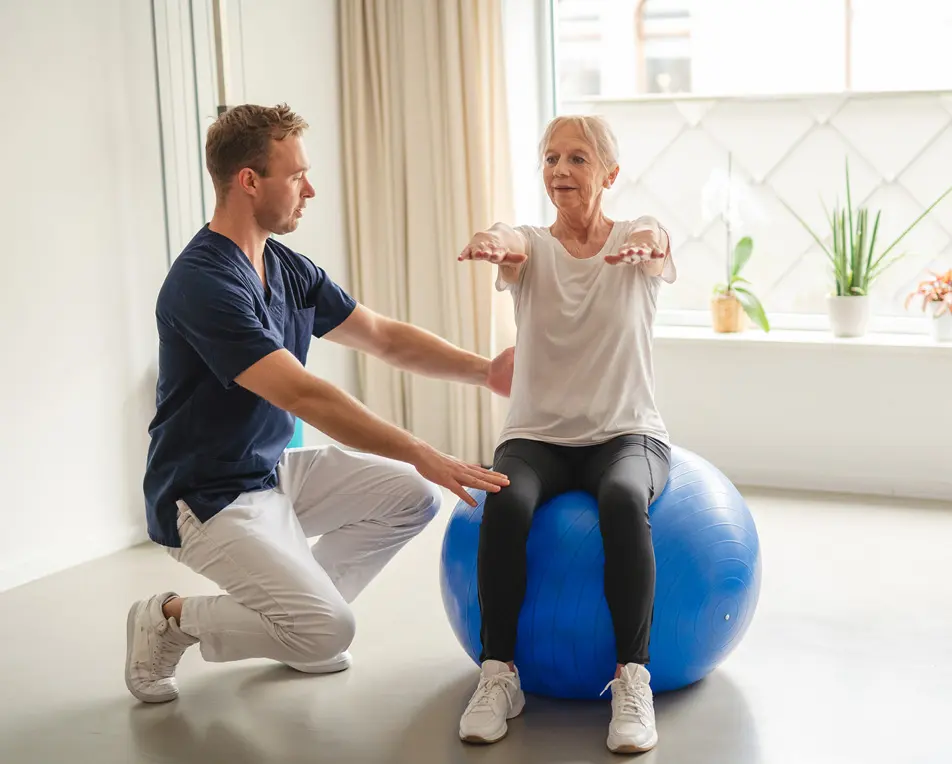 Vrouw zit op een blauwe yogabal en man helpt haar.