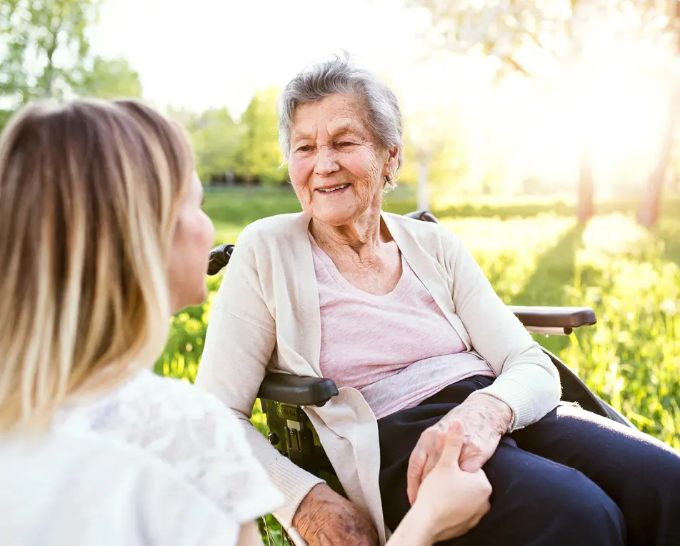 Vrouw houdt hand vast van oudere vrouw in rolstoel.