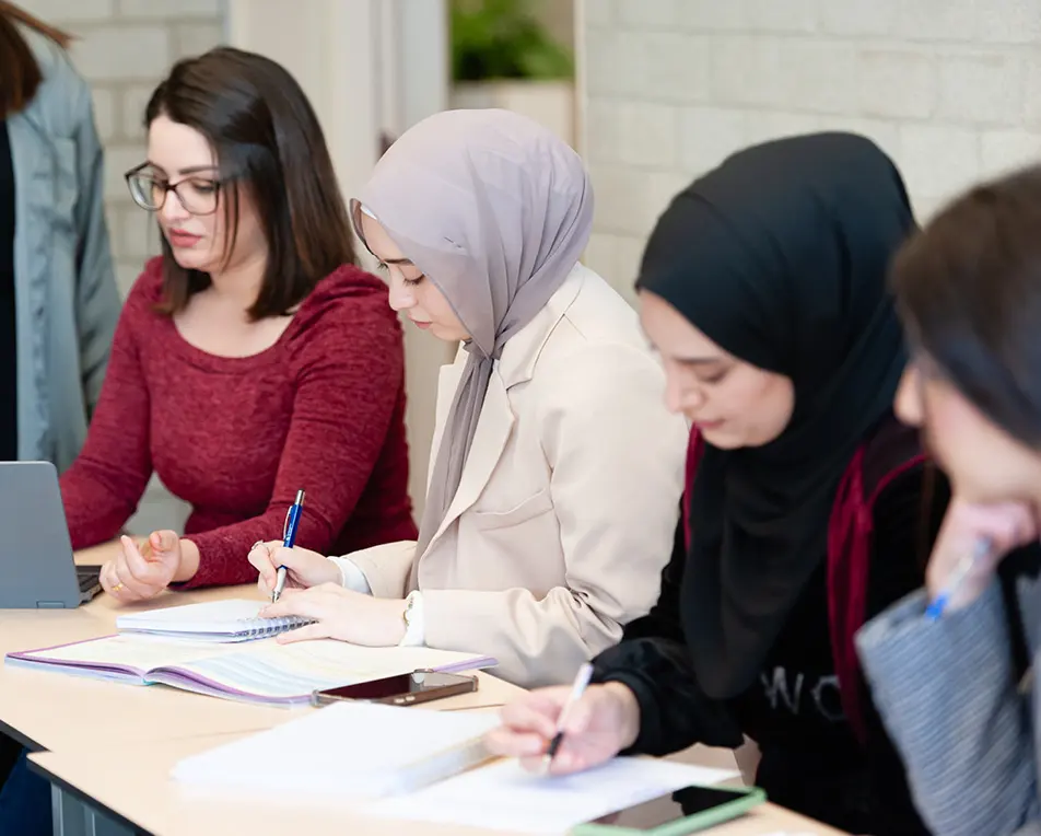 Groep vrouwen zitten aan tafels en zijn aan het schrijven.
