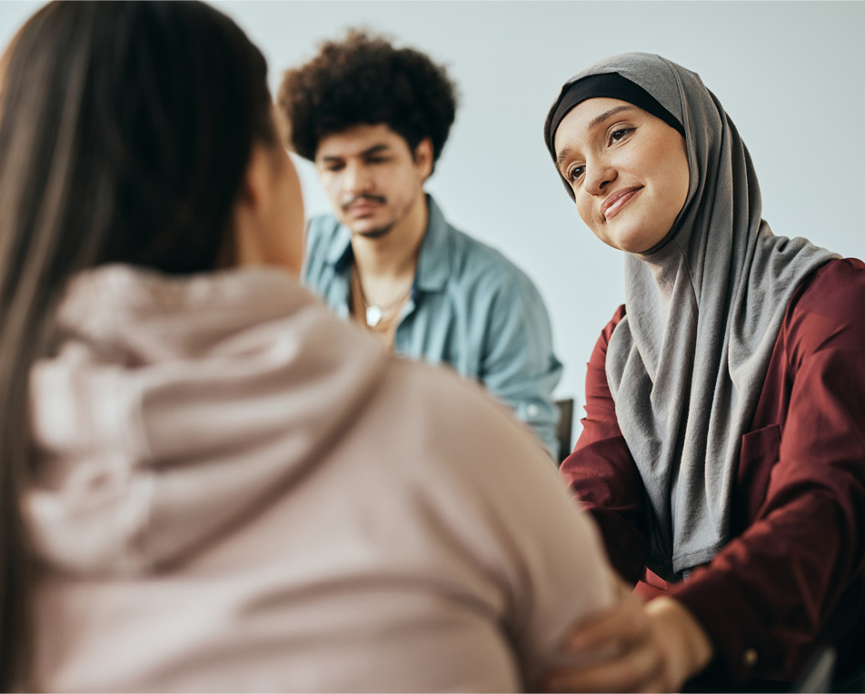 drie personen die met elkaar in gesprek zijn, een met hoofddoek, een met krullen en van een zie je alleen de rug.