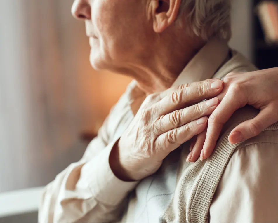 Vrouw legt haar hand op de schouder van een oudere vrouw, zei houdt deze hand vast.