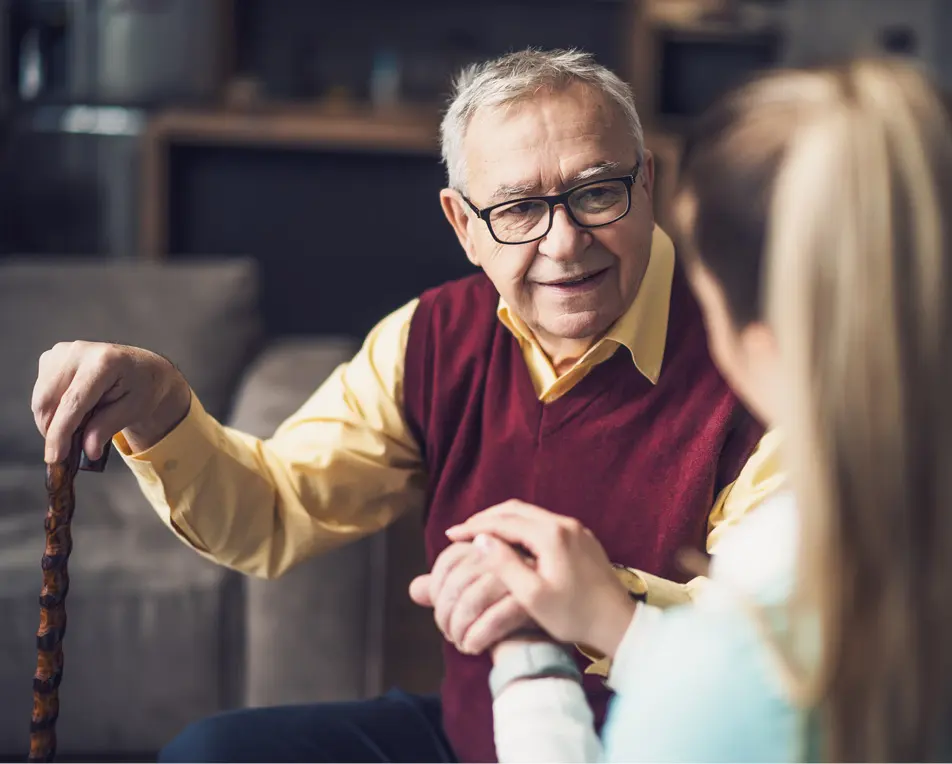 Oudere man zit, een vrouw houdt zijn hand vast.