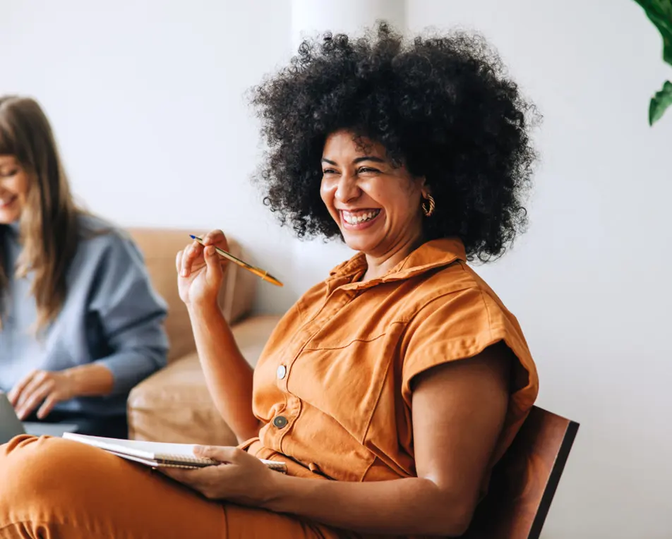 Vrouw in oranje pak lacht en zit in een lichte ruimte