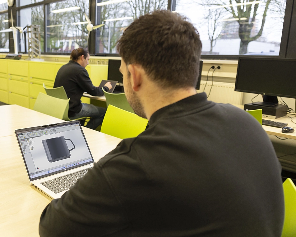 Vier personen staan rond een tafel en bespreken bouw- of technische blauwdrukken, met kantoorartikelen zoals pennen en plakbriefjes op tafel.