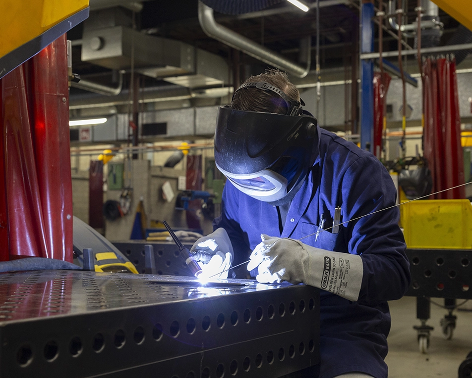 Een persoon met lashelm en handschoenen last in een werkplaats