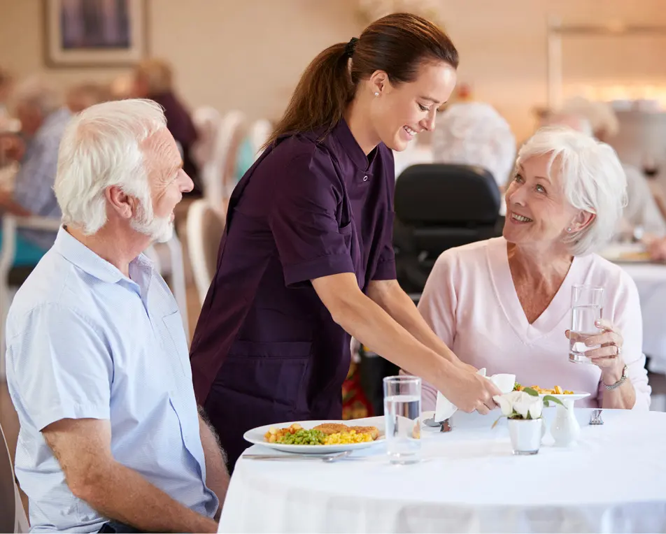 restaurant met in de voorgrond 2 personen die aan het eten zijn en een persoon die hulp biedt.