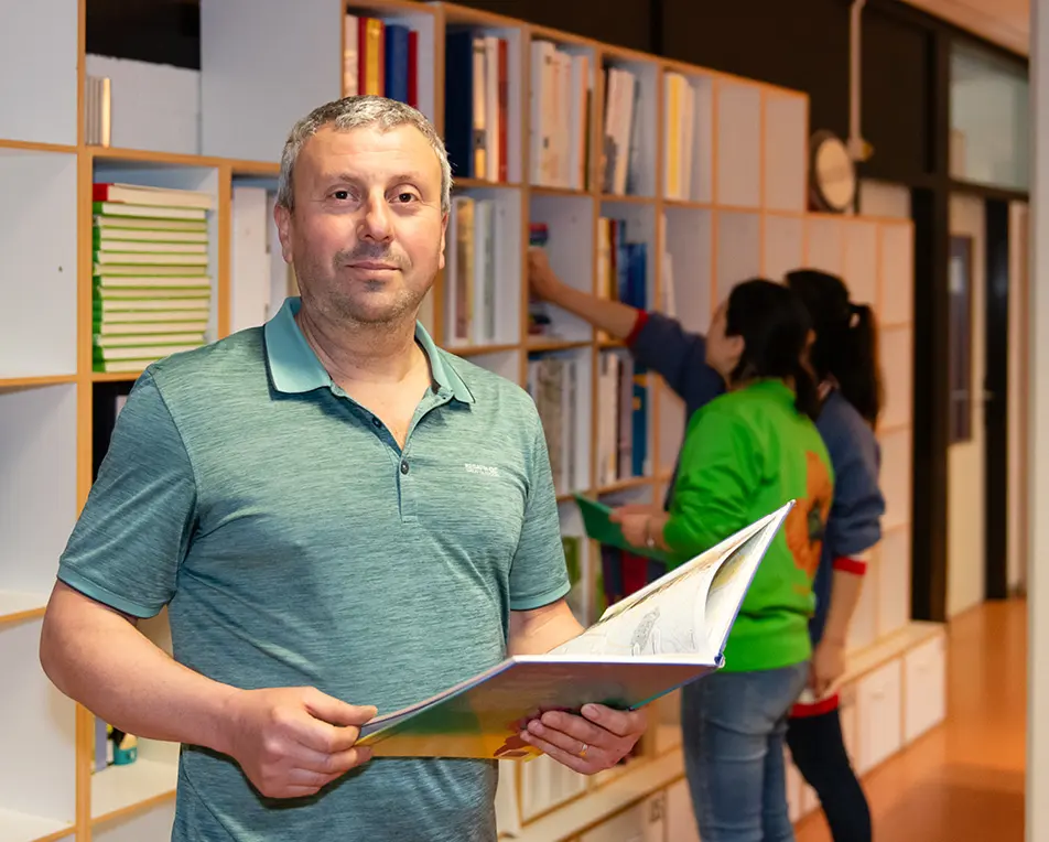 Man in een groene polo houdt een open boek vast voor een boekenkast