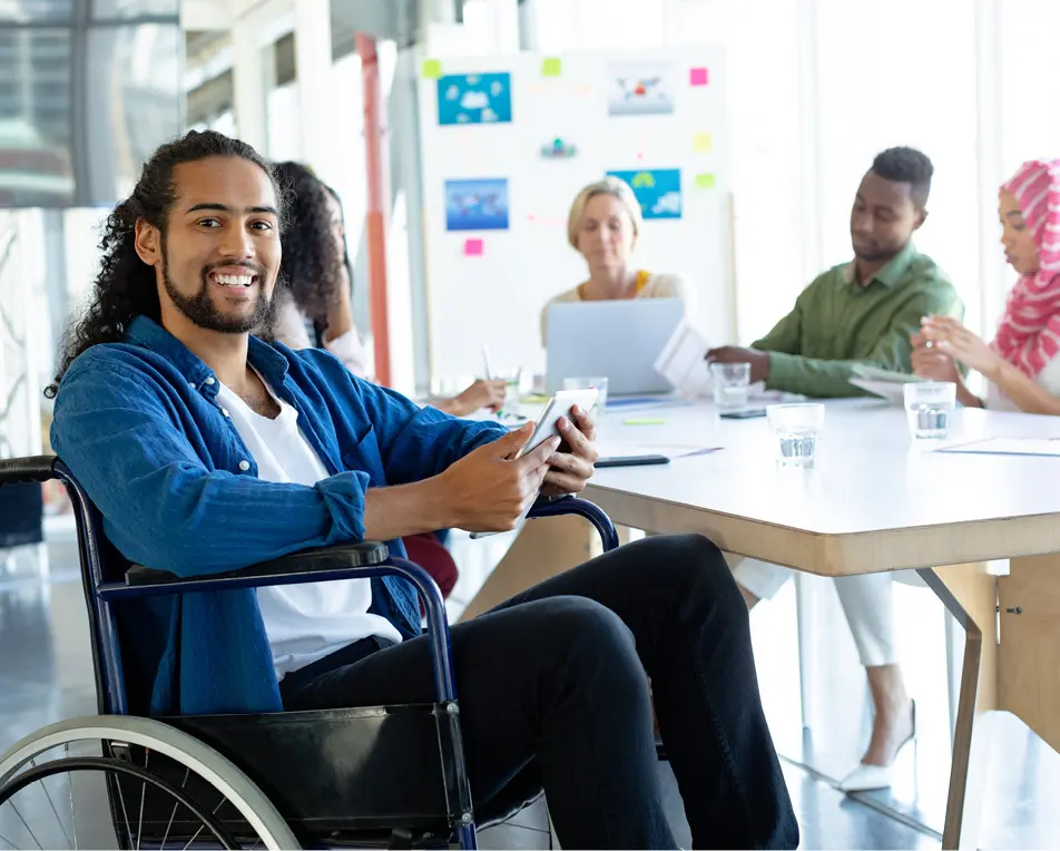 Groep personen zitten in een lichte vergaderruimte, op de voorgrond zit een man in een rolstoel.