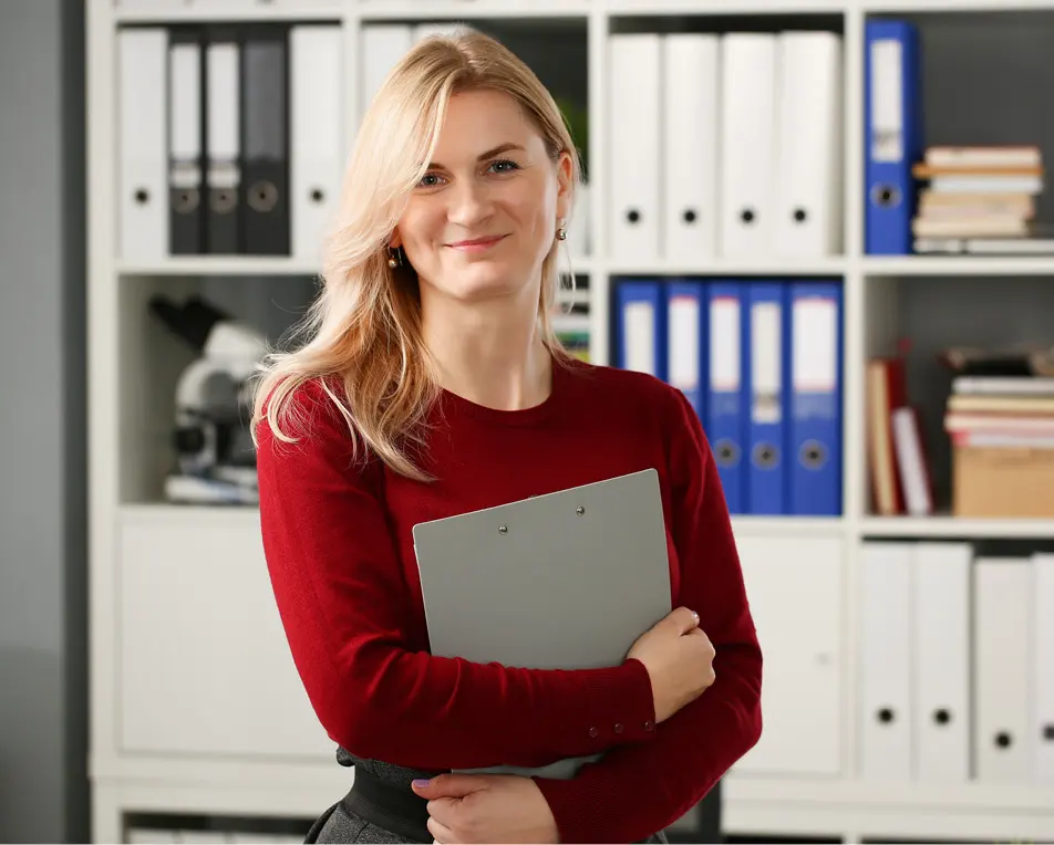 Blonde vrouw staat met papieren in haar hand voor een kast met mappen.