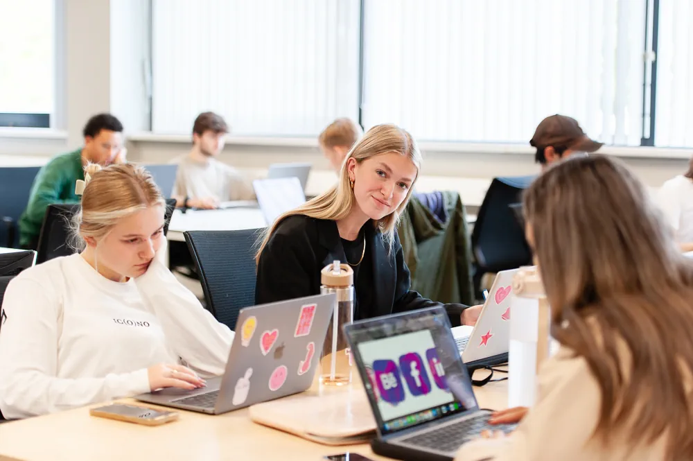 Klaslokaal waar studenten werken achter hun laptop.