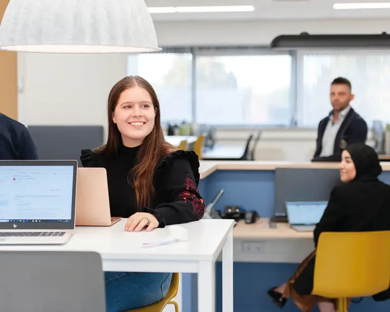 Kantoorruimte met witte tafels en een vrouw die aan het werk is.
