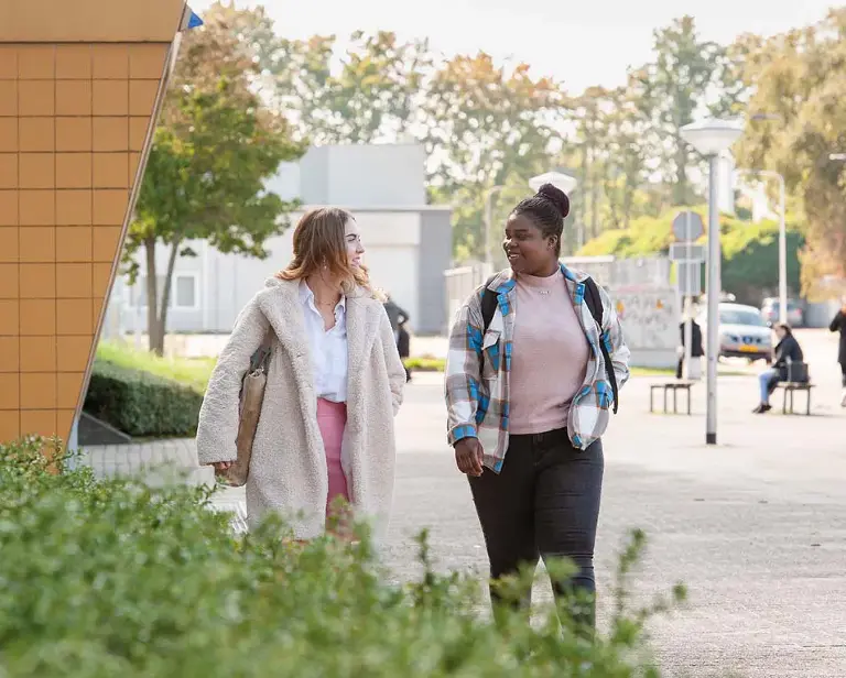 Twee vrouwen lopen op een groot plein.