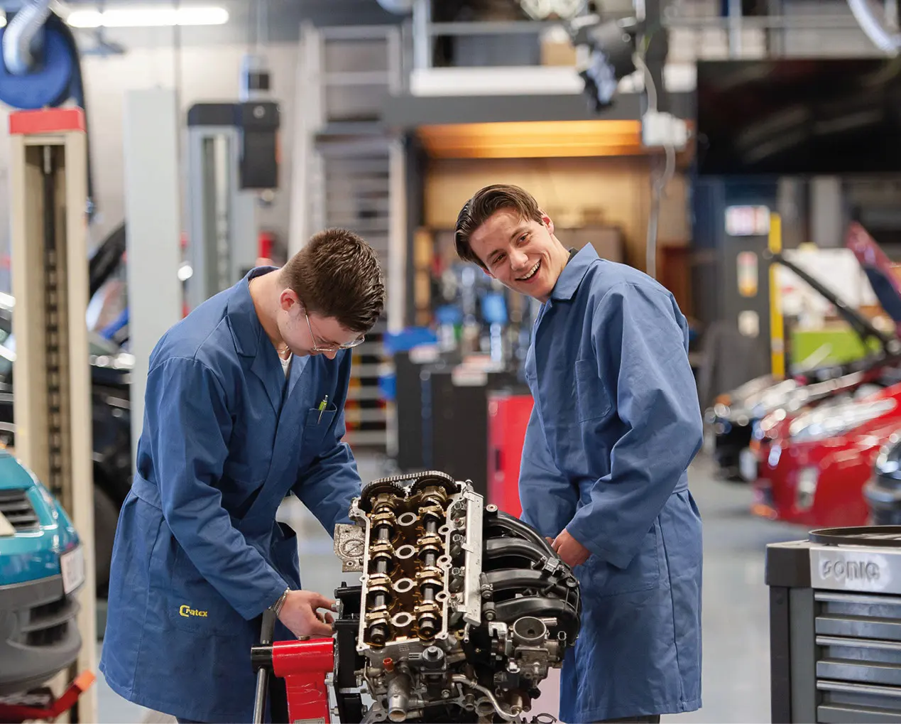 Twee jongens in blauwe overal aan het werk in autogarage.