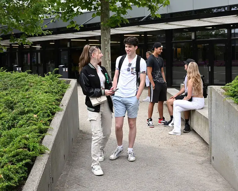 Vijf jongeren buiten, in een omgeving met struiken en bomen.