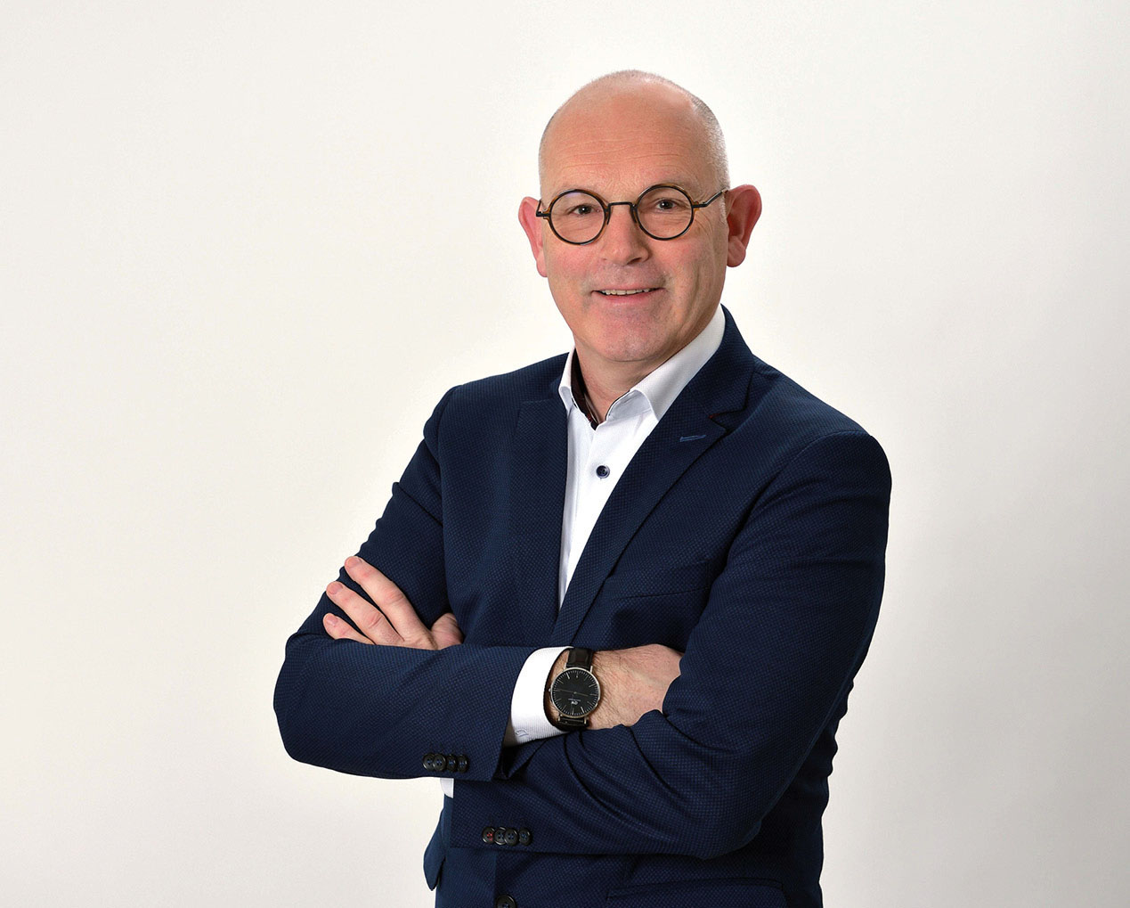 Man met net pak en bril voor een witte achtergrond.