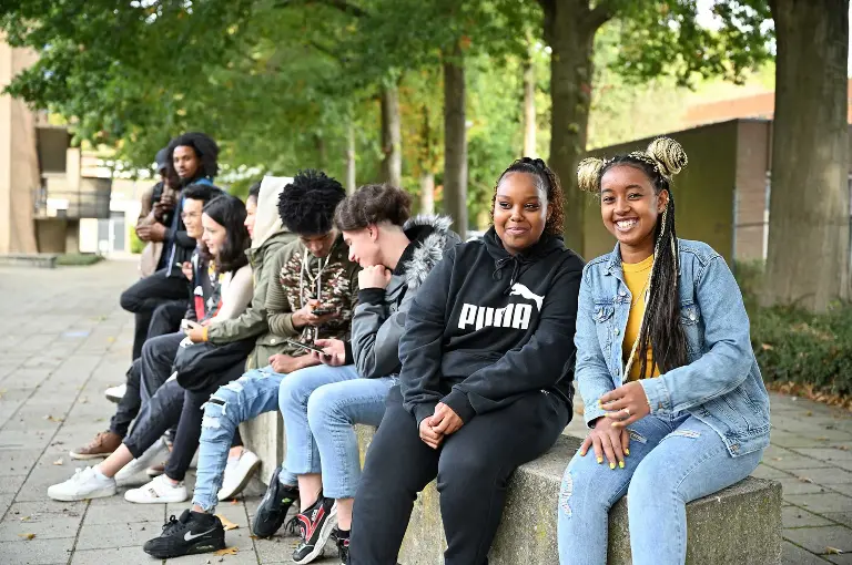 Schoolplein waar studenten op betonnen blokken zitten.