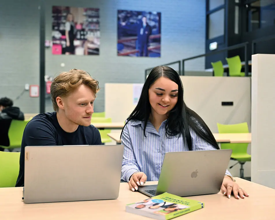 Twee personen zitten aan een tafel met laptops.