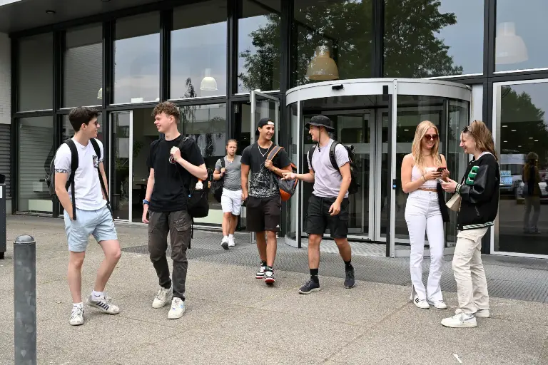 Jongeren voor een gebouw met veel ramen.