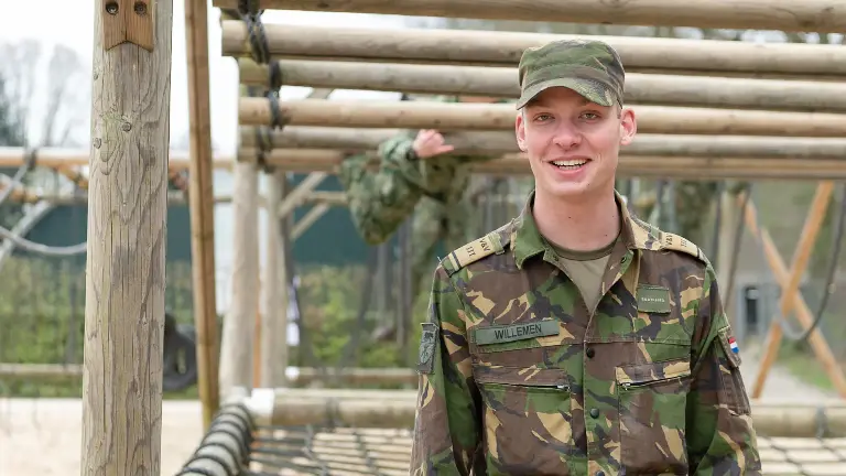 Man met een camouflage jas staat voor hindernisbaan.