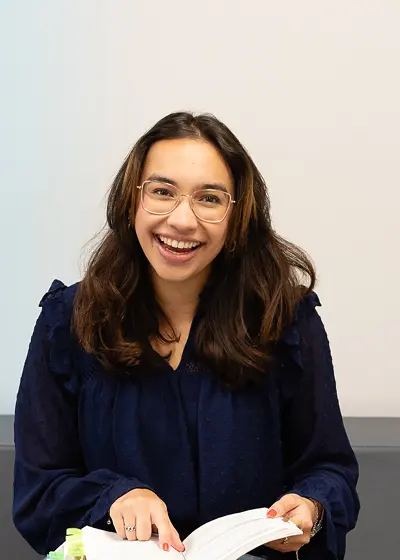 Persoon zit op een beklede bank met een open boek in de hand.