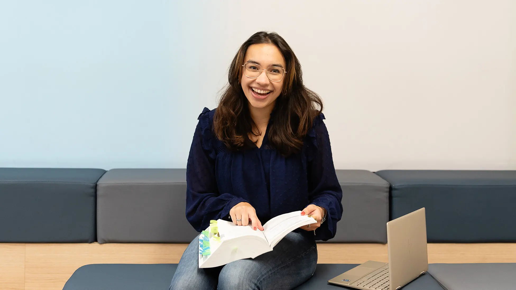 Persoon zit op een beklede bank met een open boek in de hand.