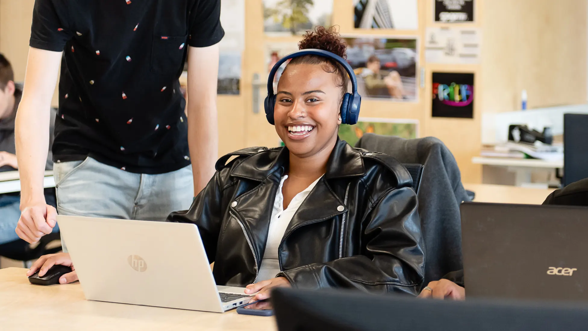 Vrouw in een klaslokaal. Ze zit achter haar laptop en heeft een koptelefoon op.