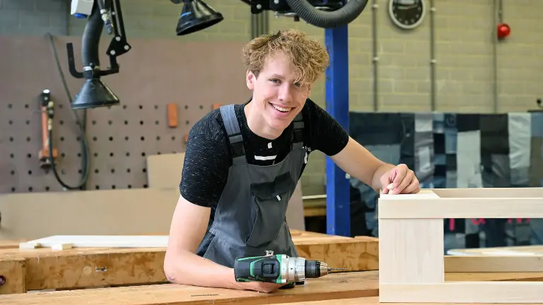 Persoon in een werkplaats met zwarte trui en grijze overal.